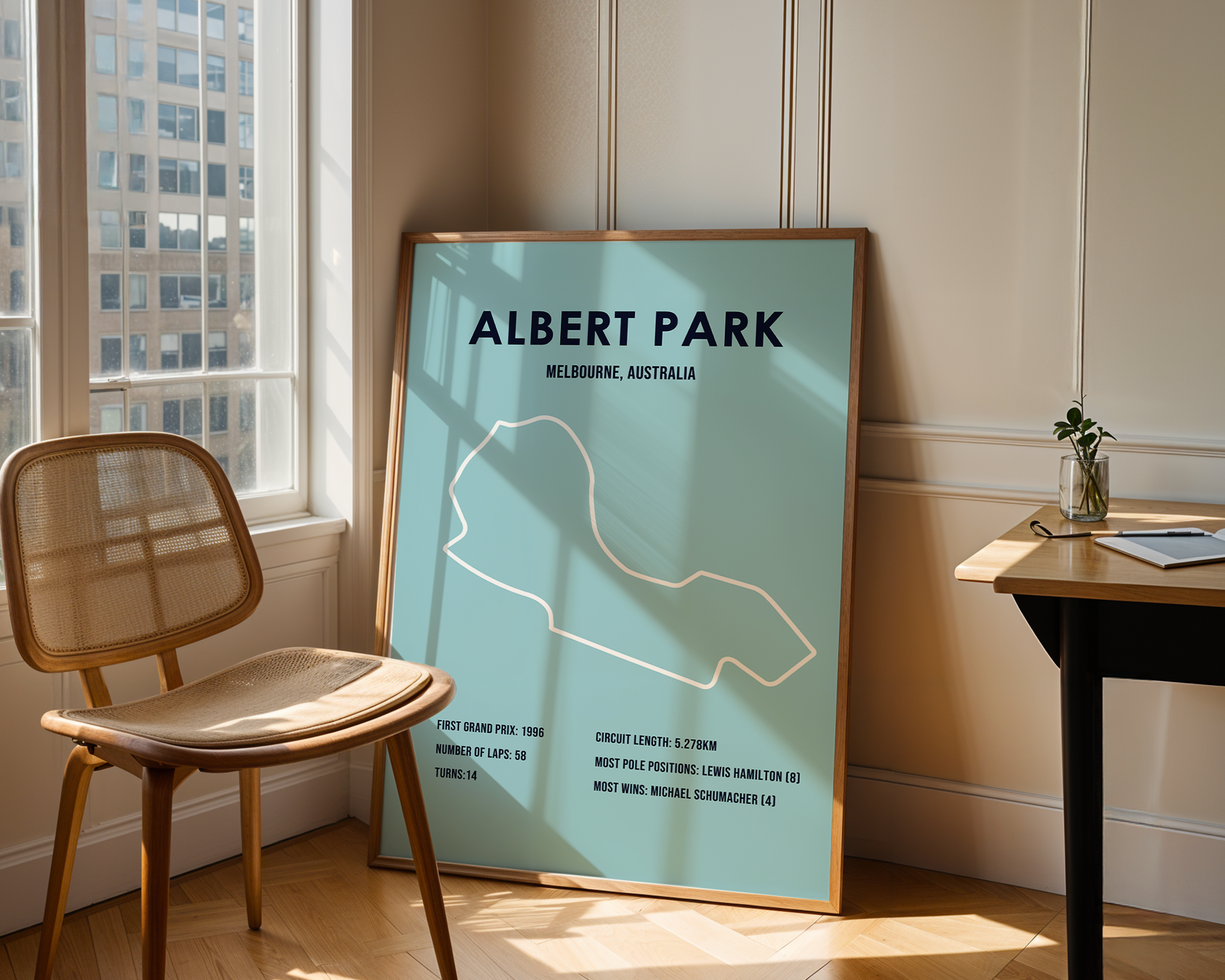 Framed poster of Albert Park circuit in Melbourne, Australia, leaning against a wall in a room with a chair and table.