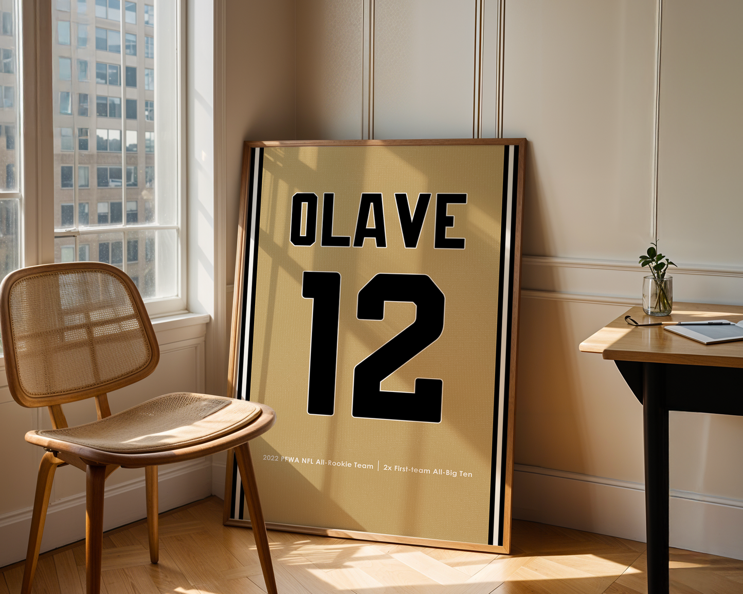 Framed poster with 'OLAVE 12' in a room with a chair and table.