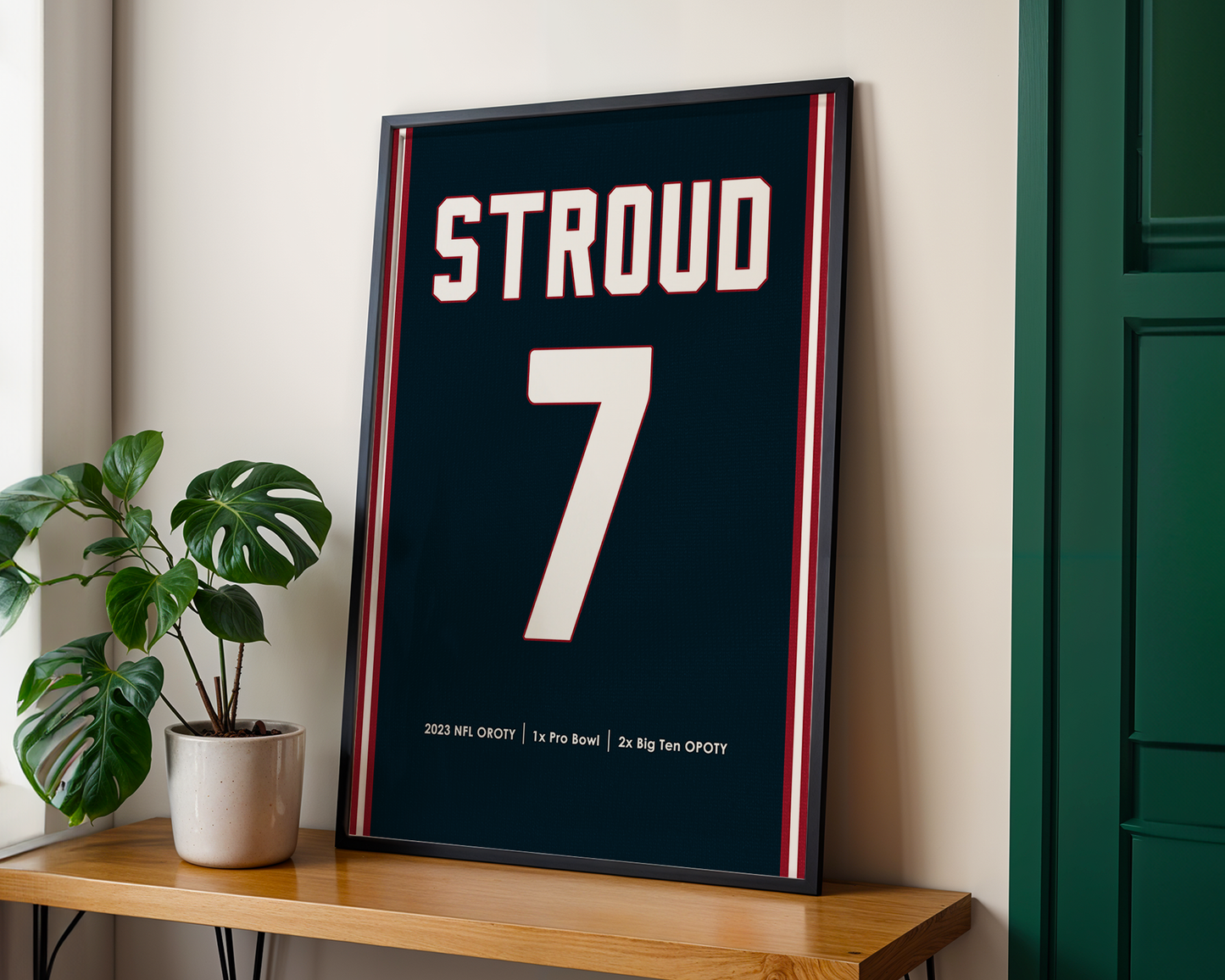 Framed sports jersey with 'STROUD' and number '7' on a wooden shelf.