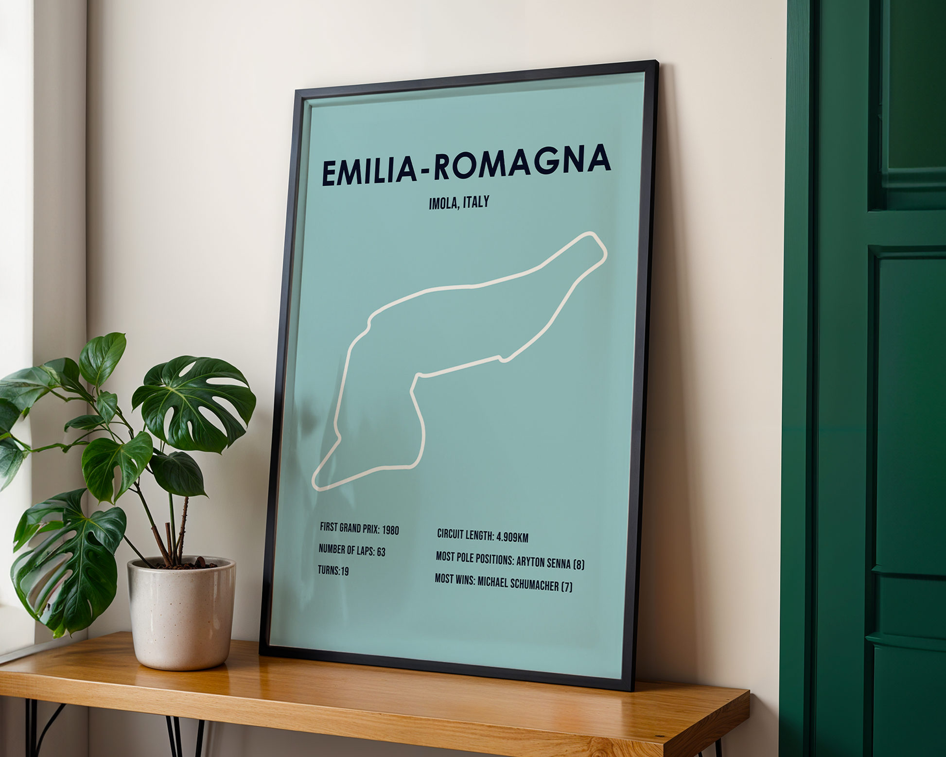 Framed poster of Emilia-Romagna race track layout on a wooden shelf with a plant.