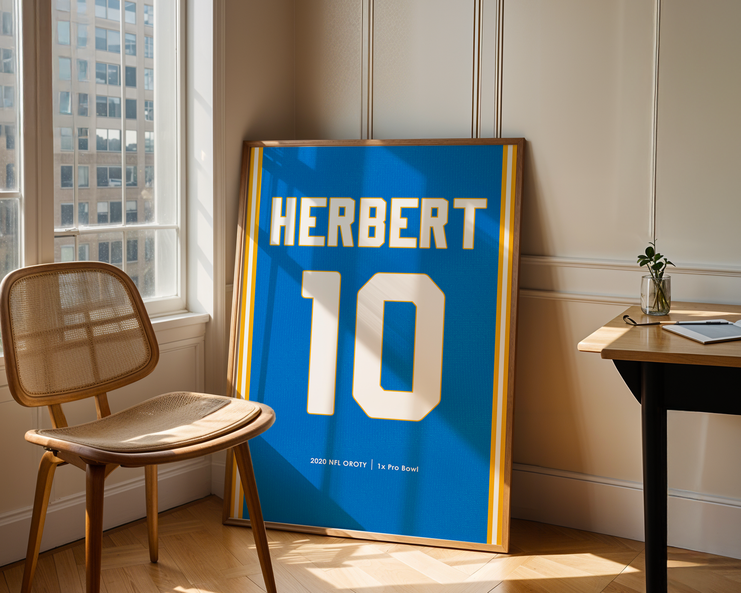 Framed sports jersey with 'HERBERT 10' on a wall in a room with a chair and table.