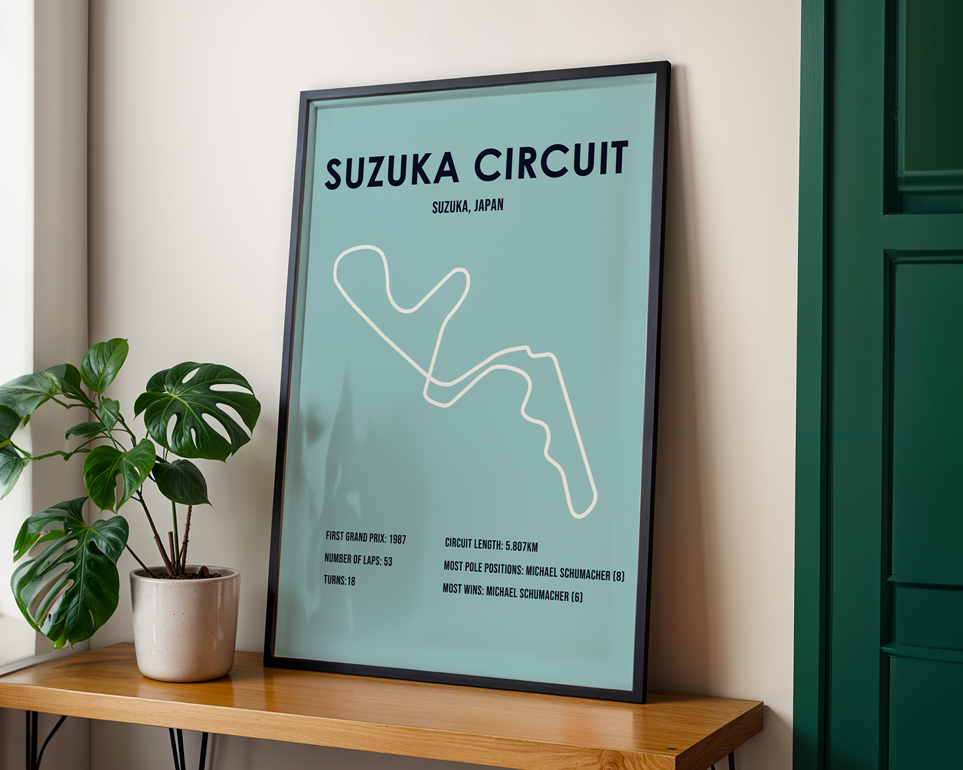 Framed poster of Suzuka Circuit on a wooden shelf with a plant.