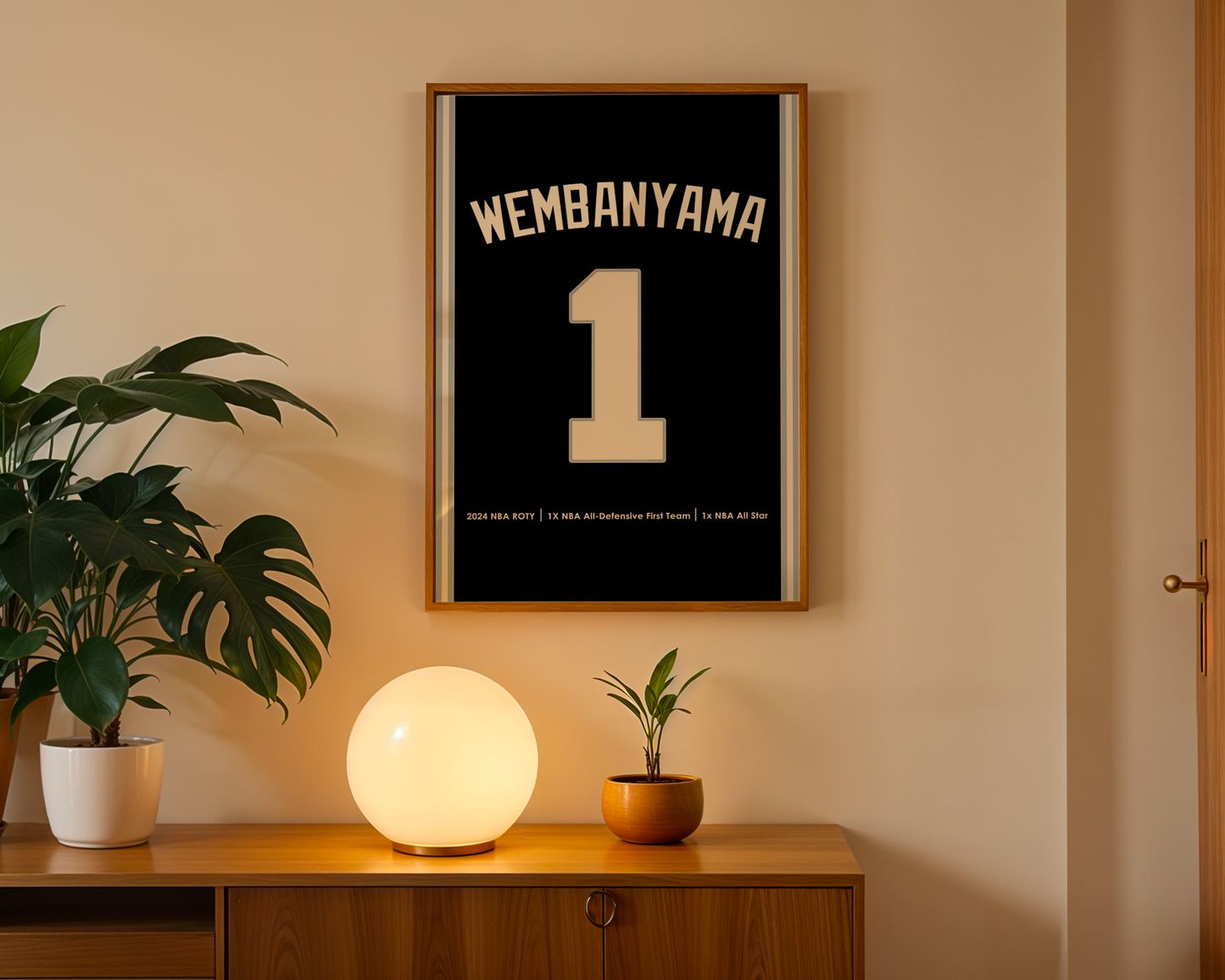 Framed artwork with 'Wembanyama 1' on a wall above a wooden cabinet with decorative items.