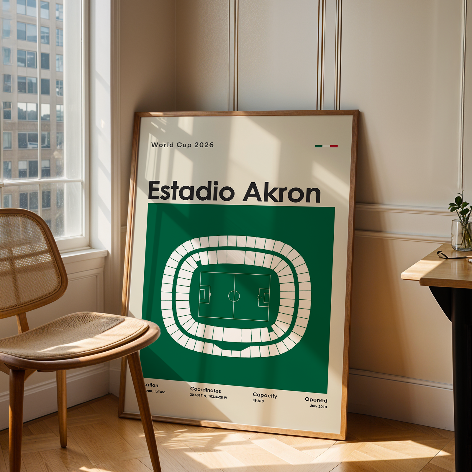 Framed poster of Estadio Akron in a room with a chair and table.