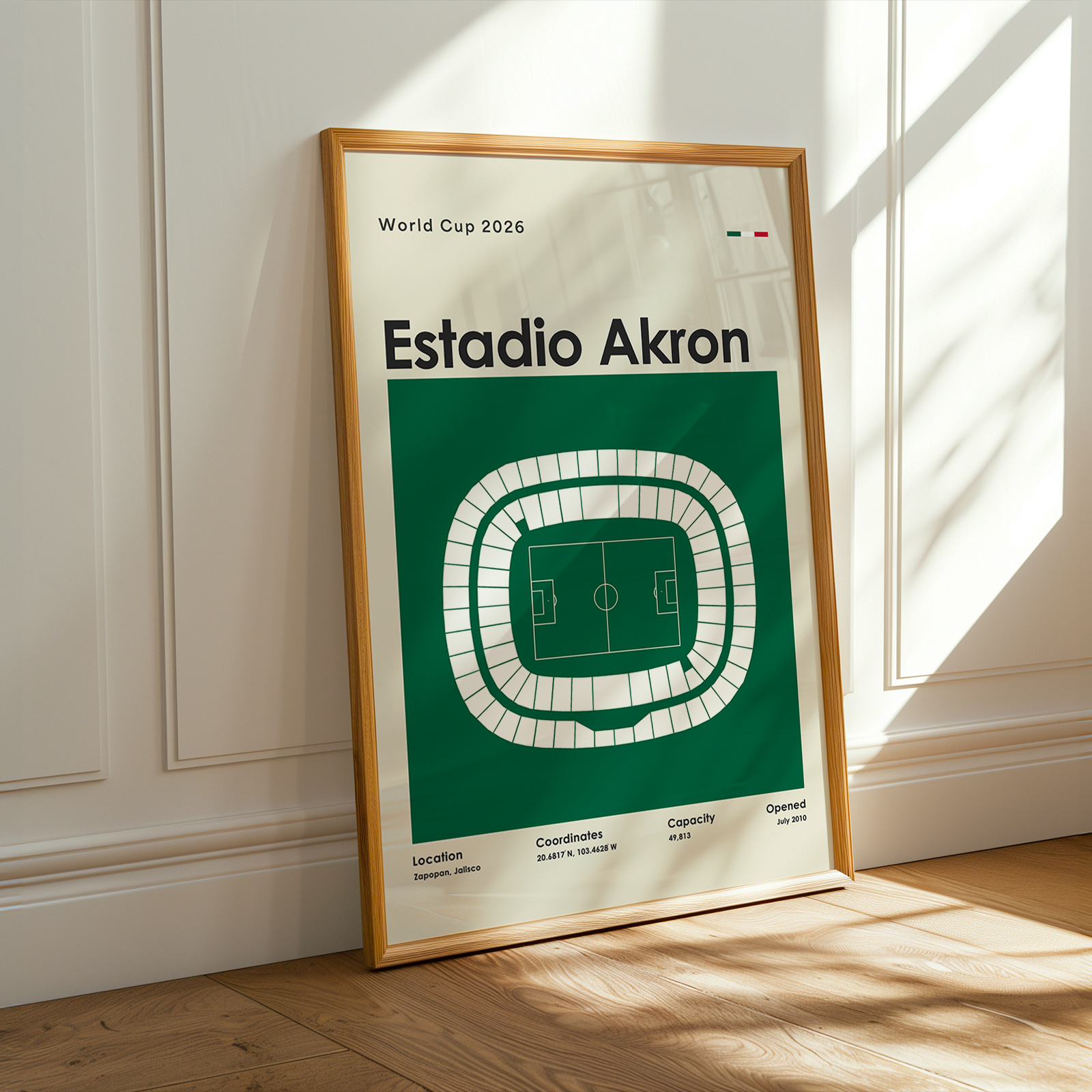 Framed poster of Estadio Akron with a green and white design, placed on a wooden floor.