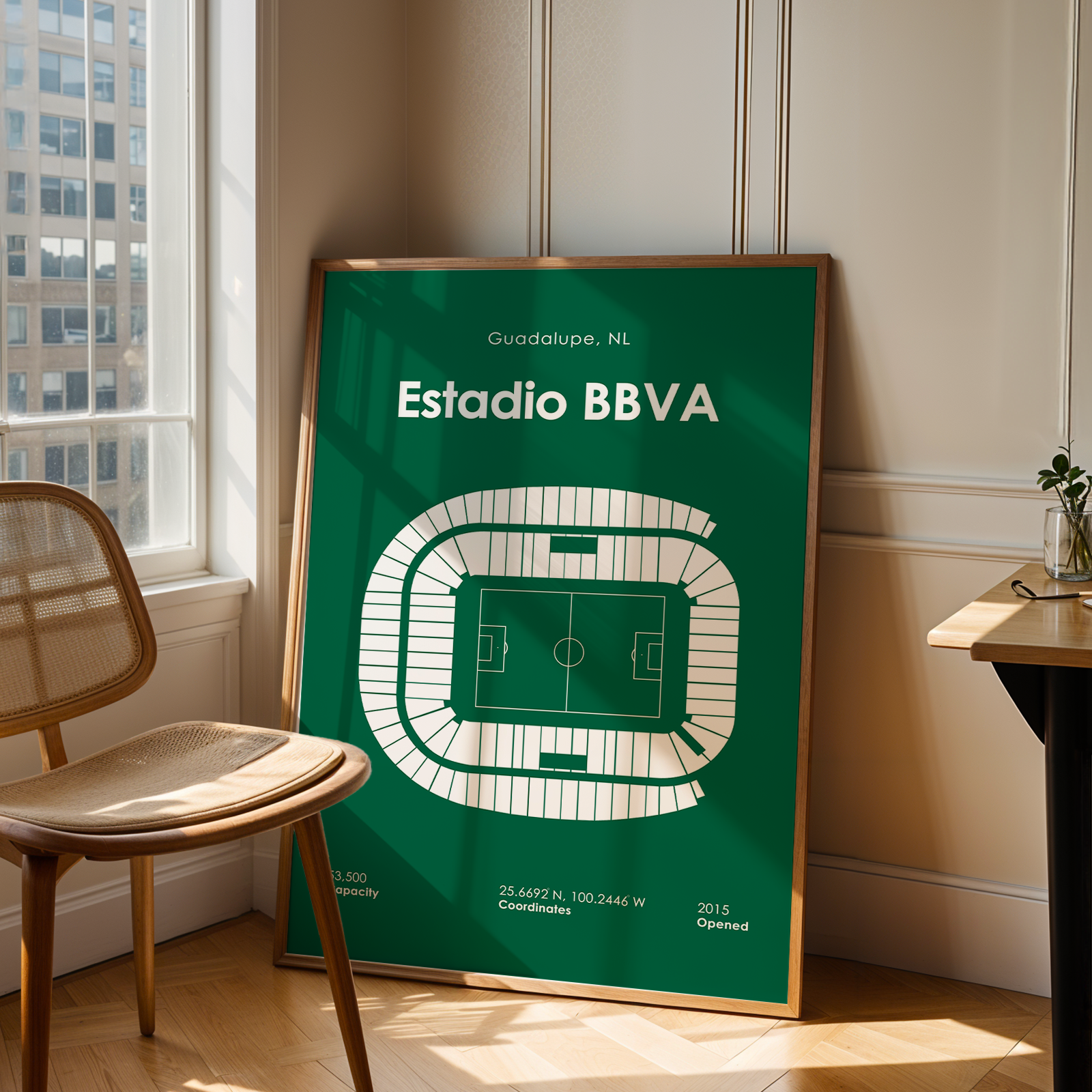 Framed poster of Estadio BBVA in a room with a chair and table.