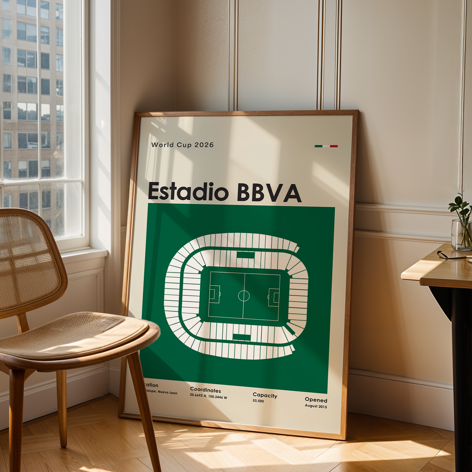 Framed poster of Estadio BBVA in a room with a chair and table.