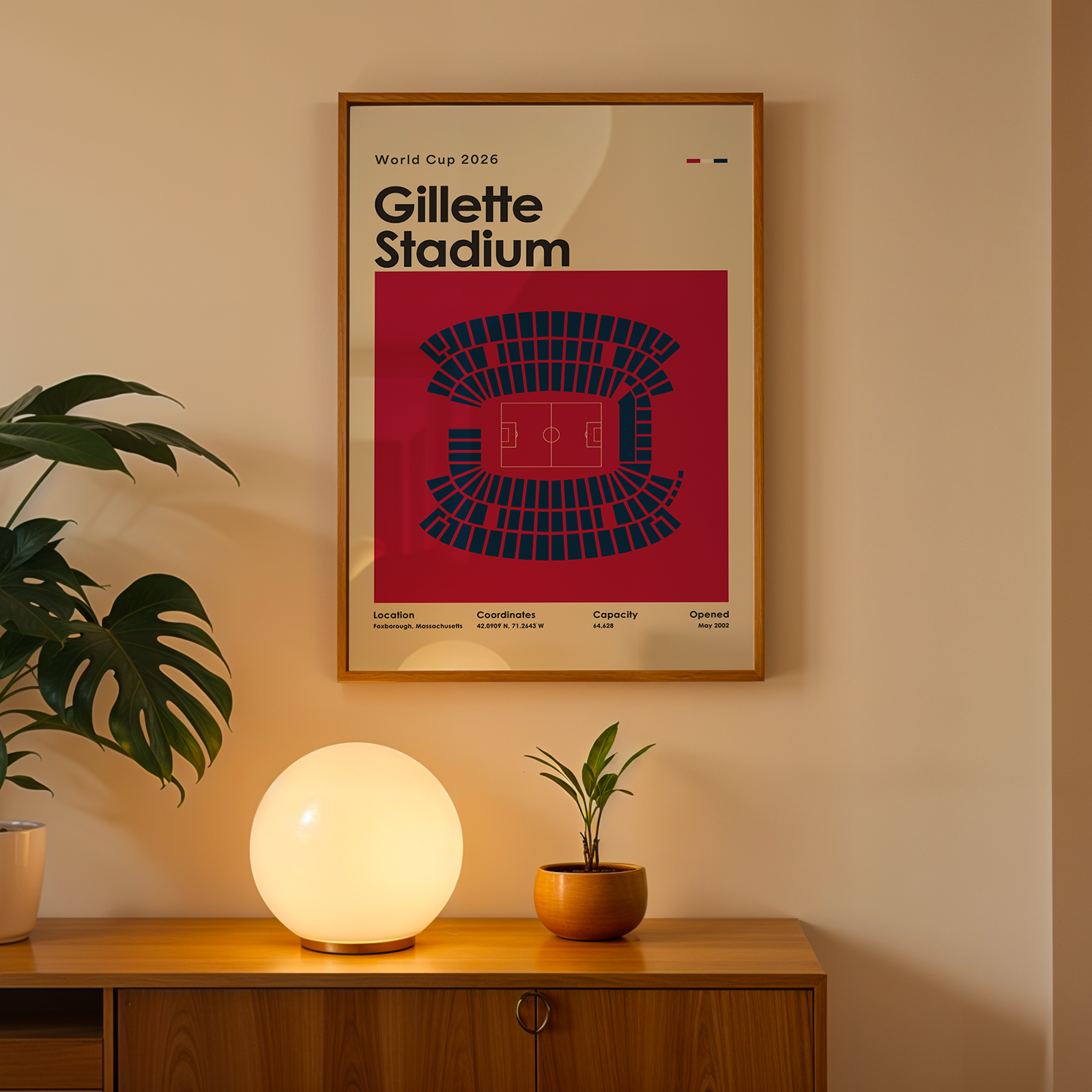 Framed poster of Gillette Stadium on a wall above a wooden cabinet with decorative items.