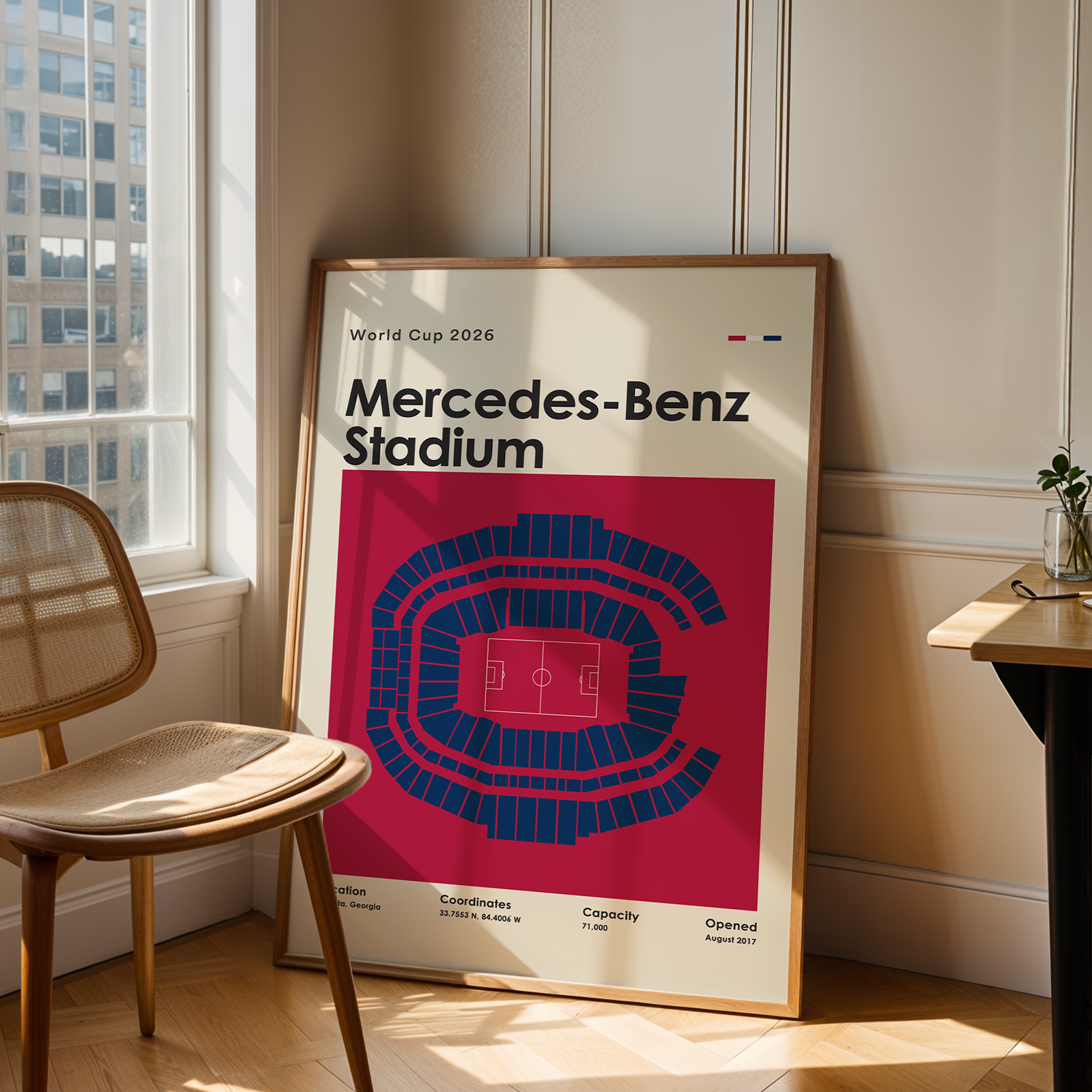 Framed poster of Mercedes-Benz Stadium in a room with a chair and table.