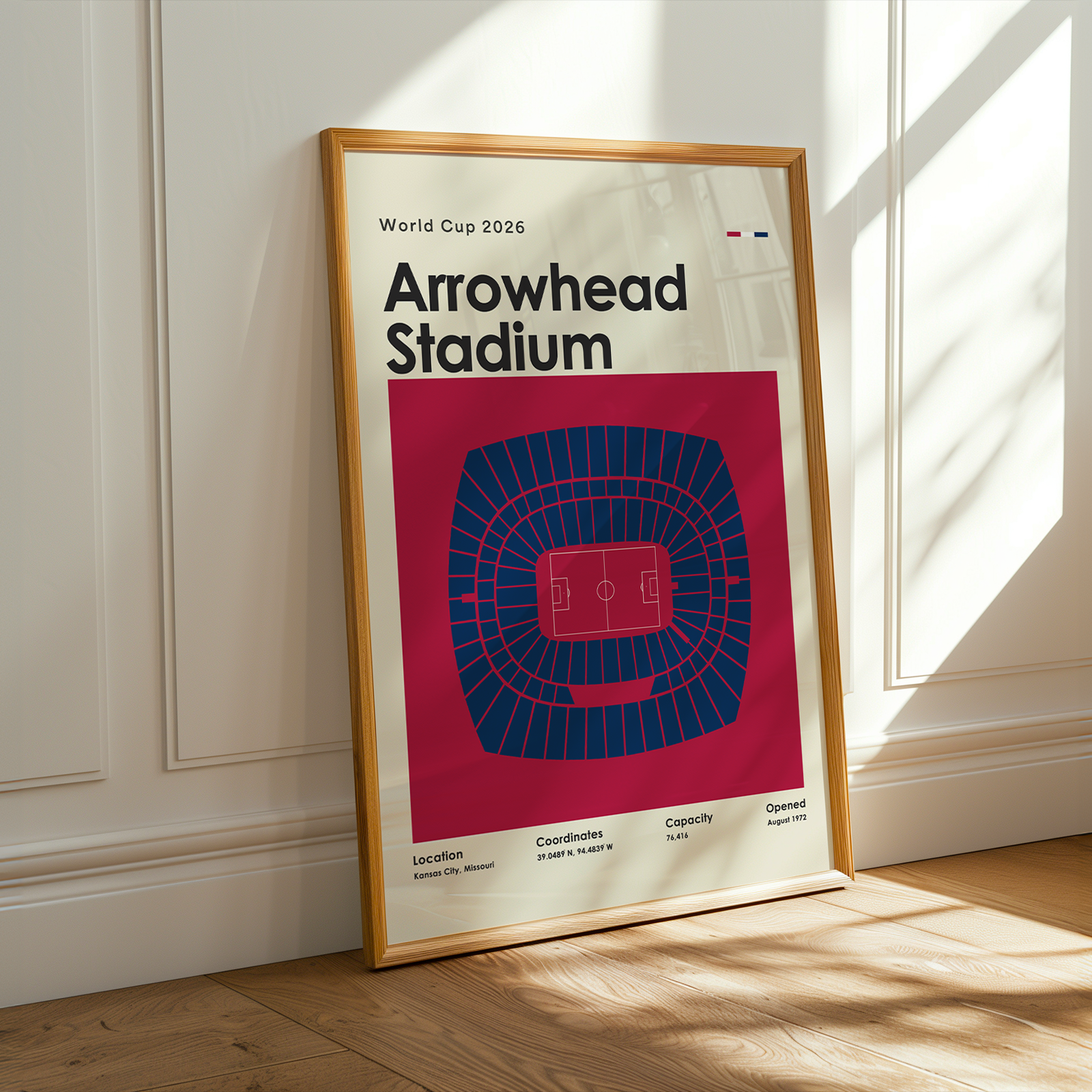 Framed poster of Arrowhead Stadium with a red and blue design, placed on a wooden floor.