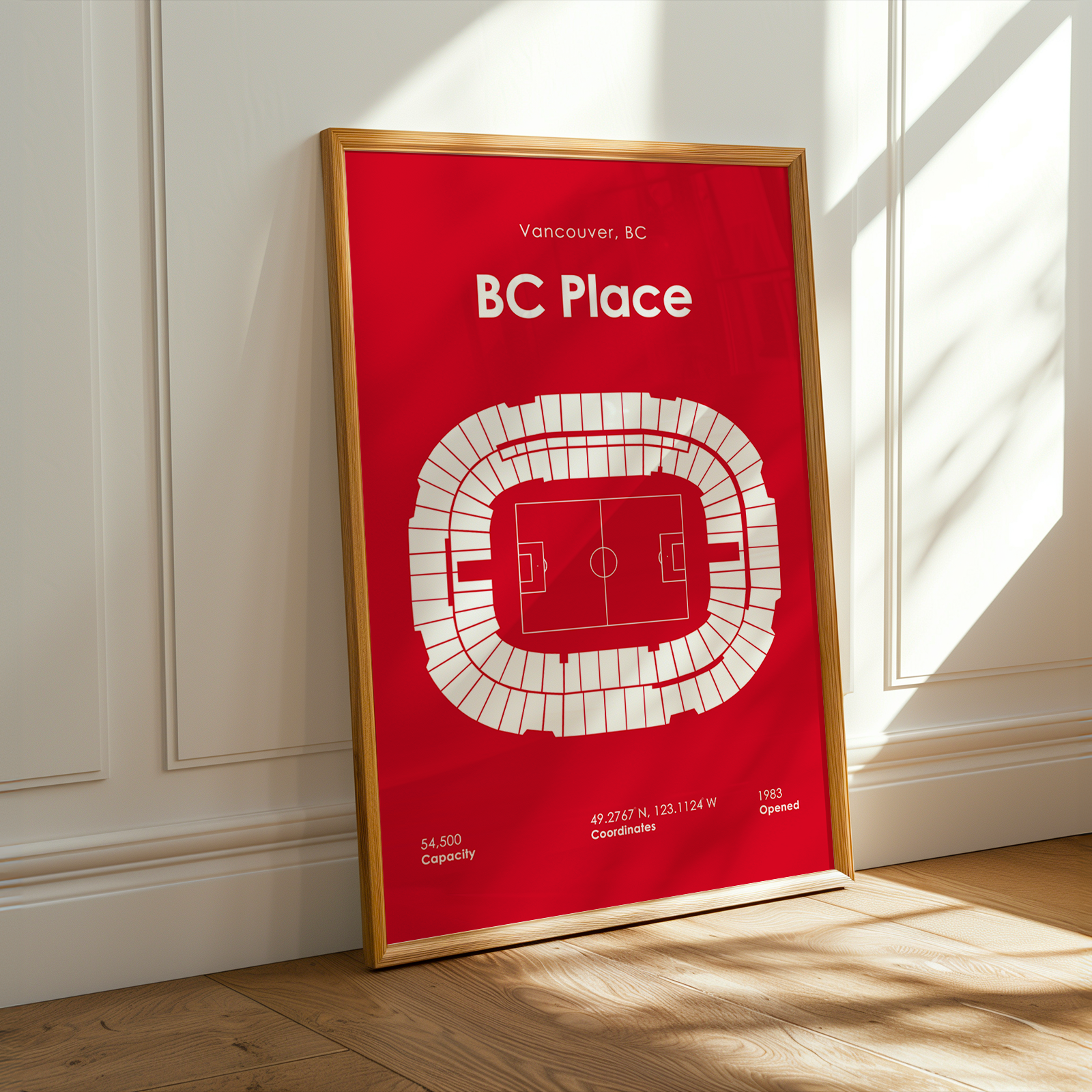 Framed poster of BC Place stadium layout on a red background, leaning against a white wall.