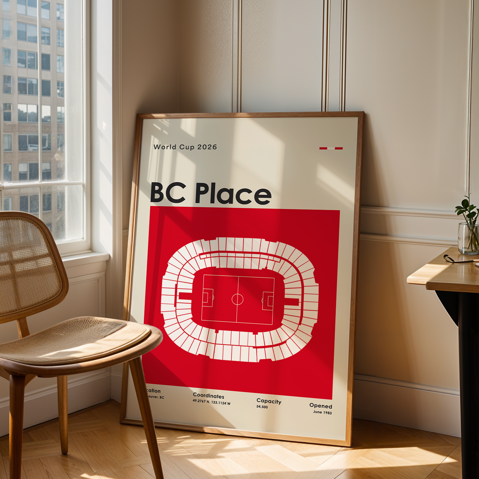 Framed poster of BC Place stadium in a room with a chair and table.