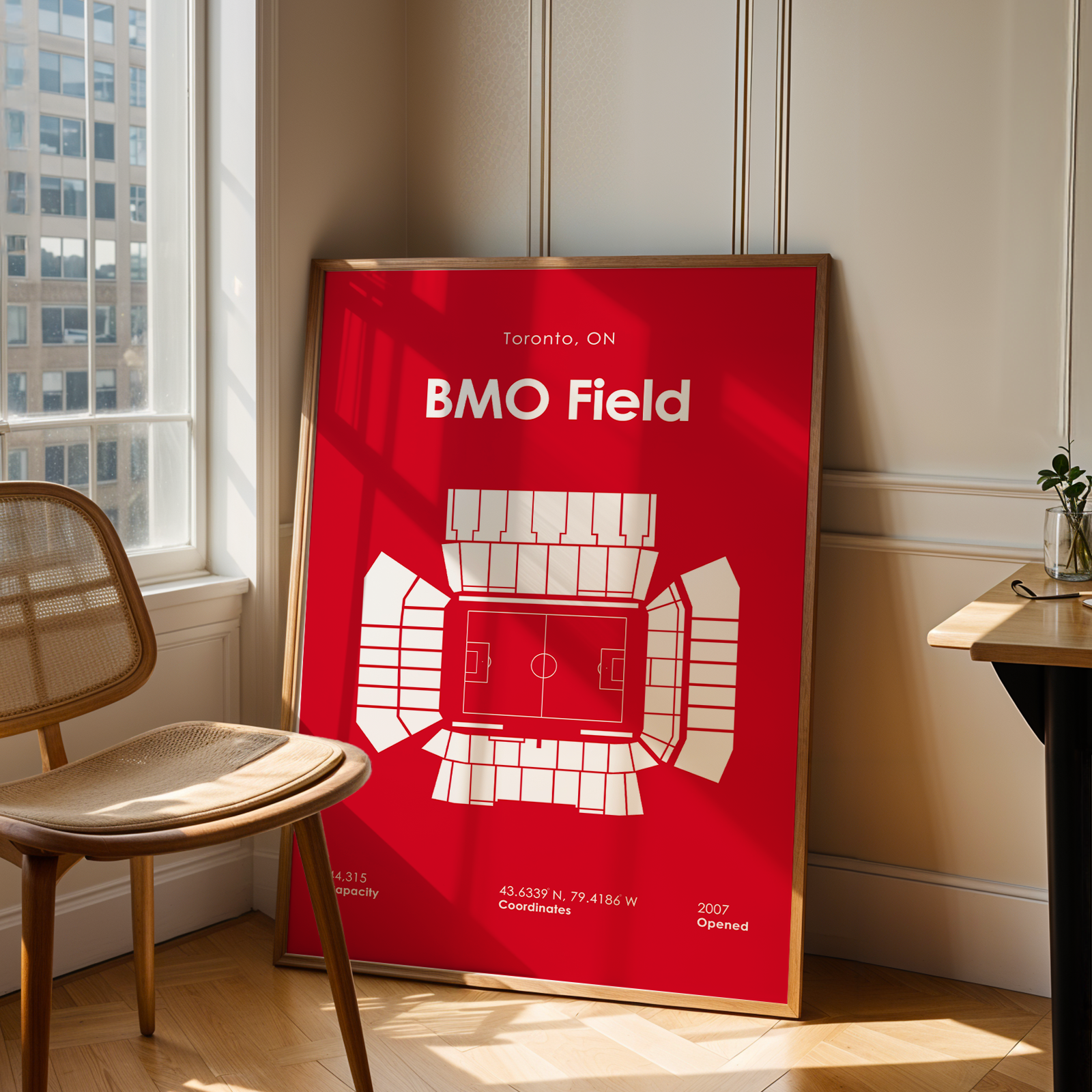 Red poster of BMO Field in Toronto, ON, leaning against a wall in a room with a chair and table.