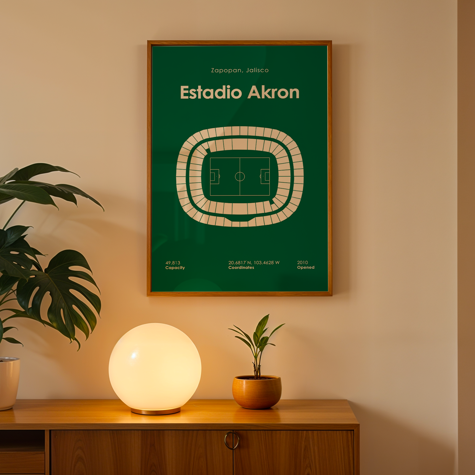Framed poster of Estadio Akron on a wall above a wooden cabinet with decorative items.