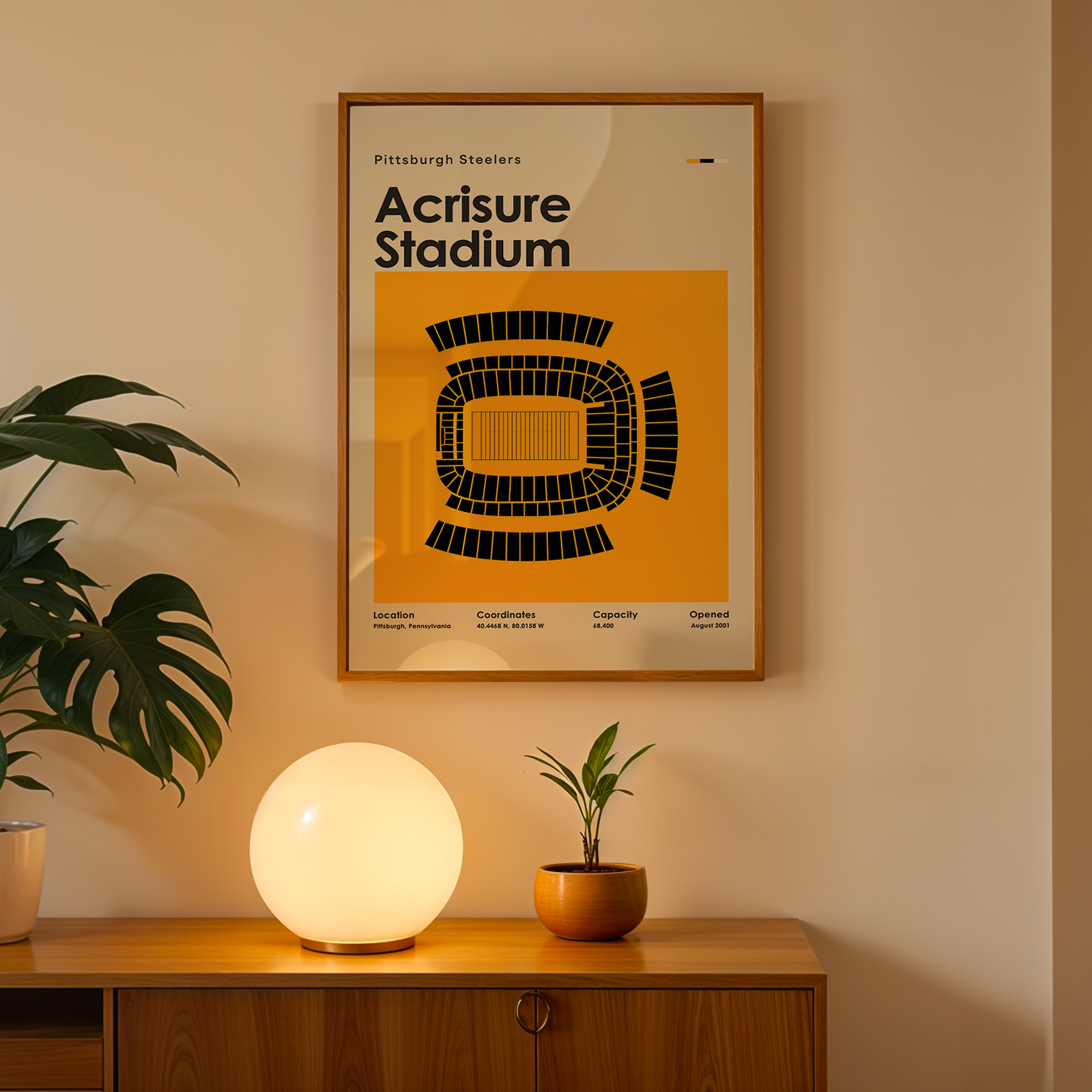 Framed poster of Acrisure Stadium on a wall above a wooden cabinet with decorative items.