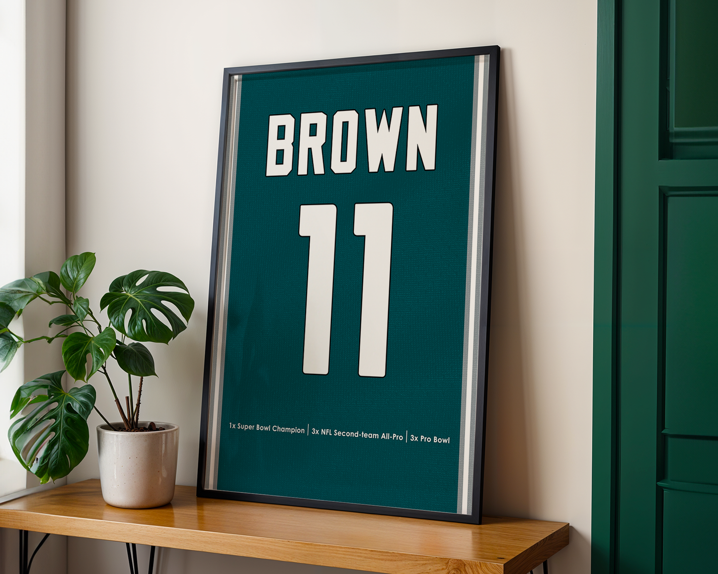Framed poster with 'Brown 11' on a wooden shelf next to a plant