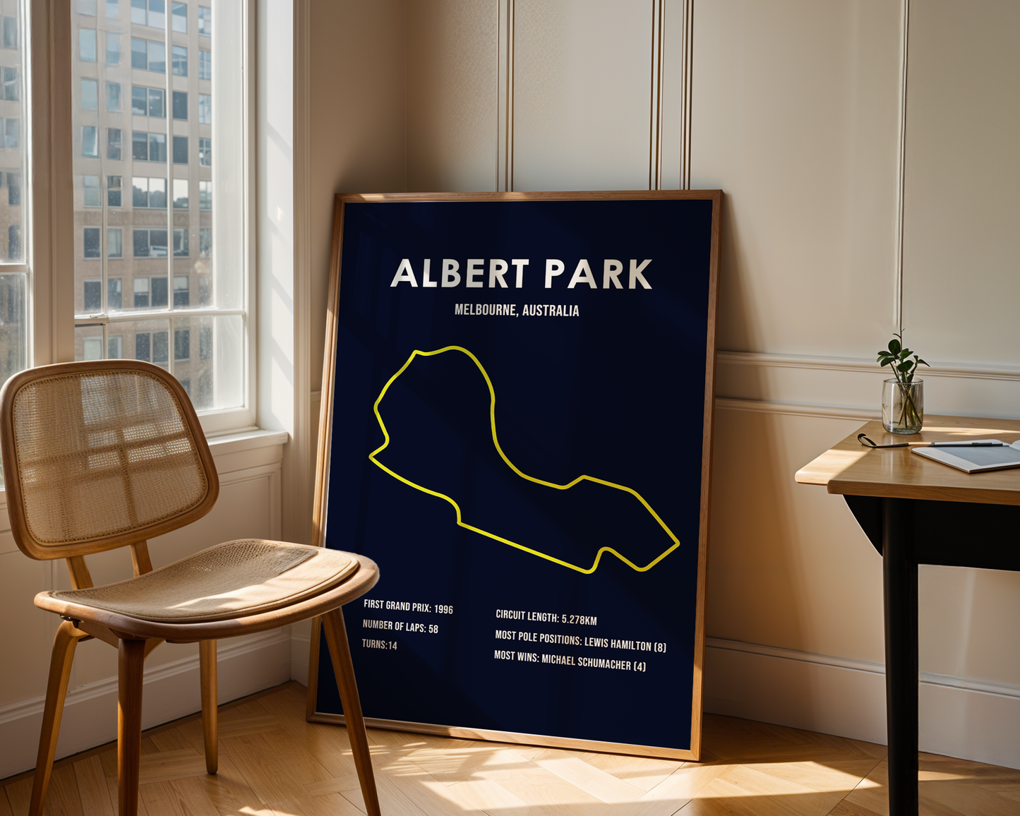 Framed poster of Albert Park circuit in Melbourne, Australia, leaning against a wall in a room with a chair and table.