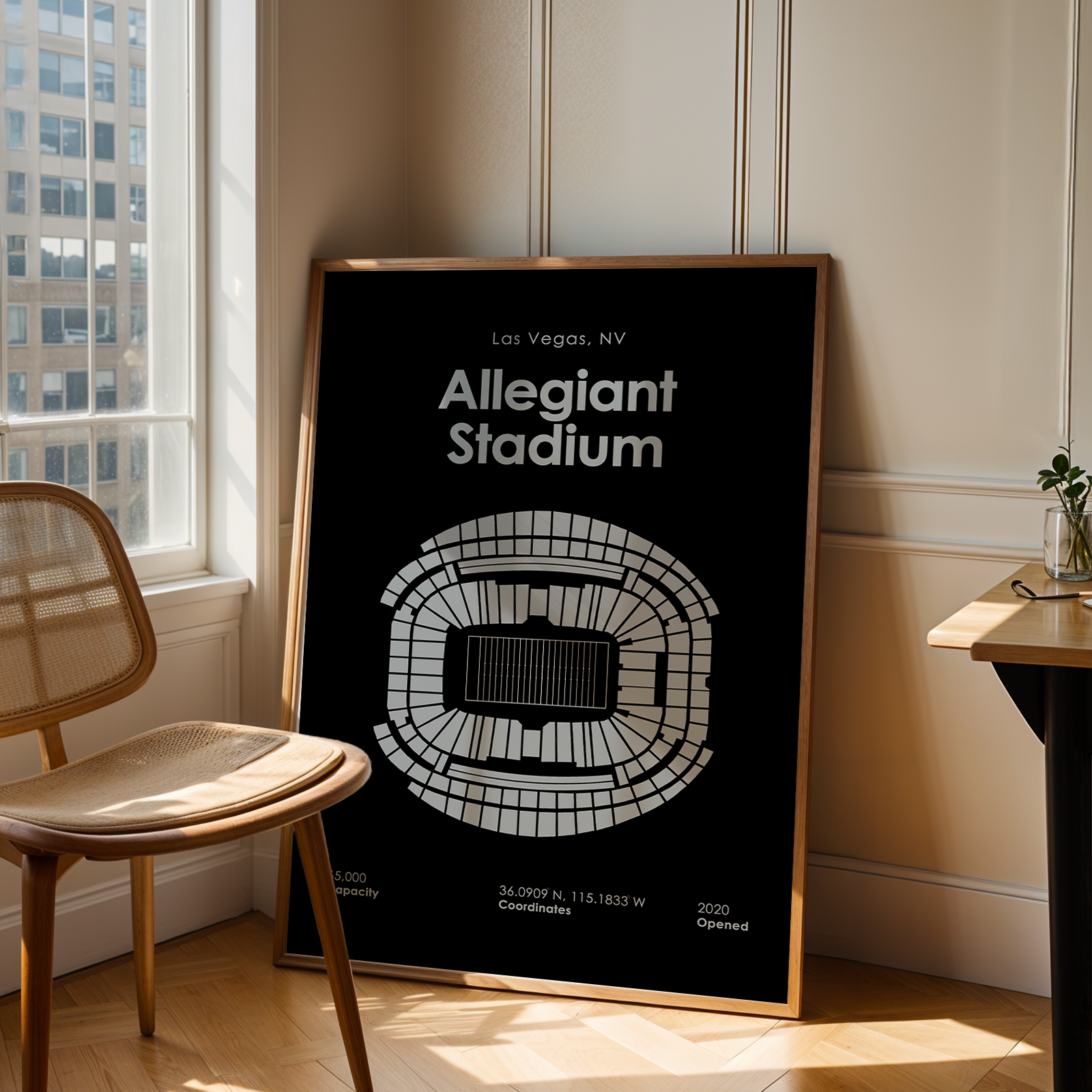 Framed poster of Allegiant Stadium in Las Vegas, NV, leaning against a wall in a room with a chair and table.