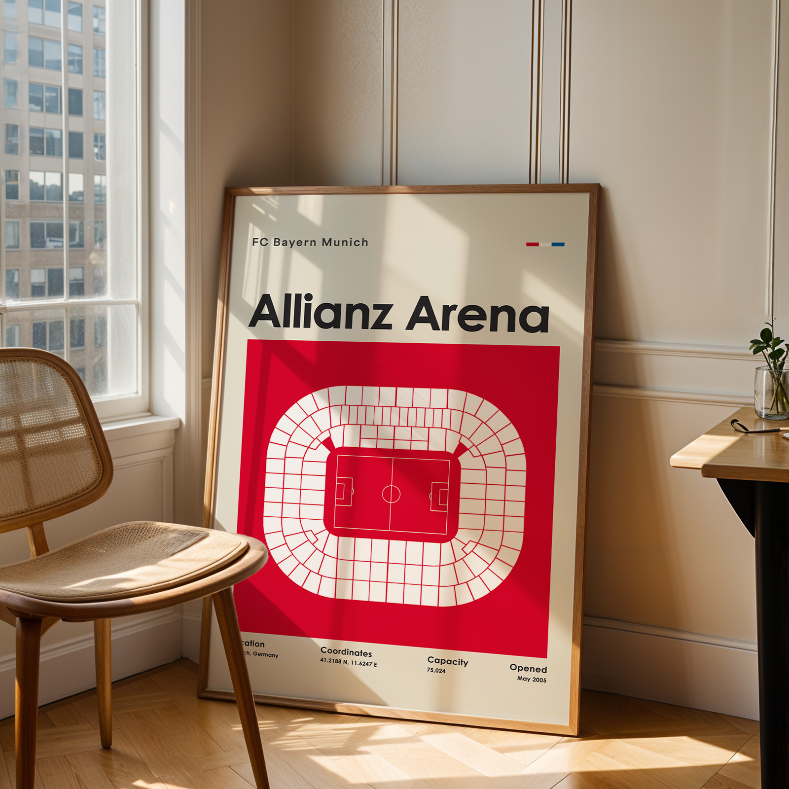 Framed poster of Allianz Arena in a room with a window and chair.