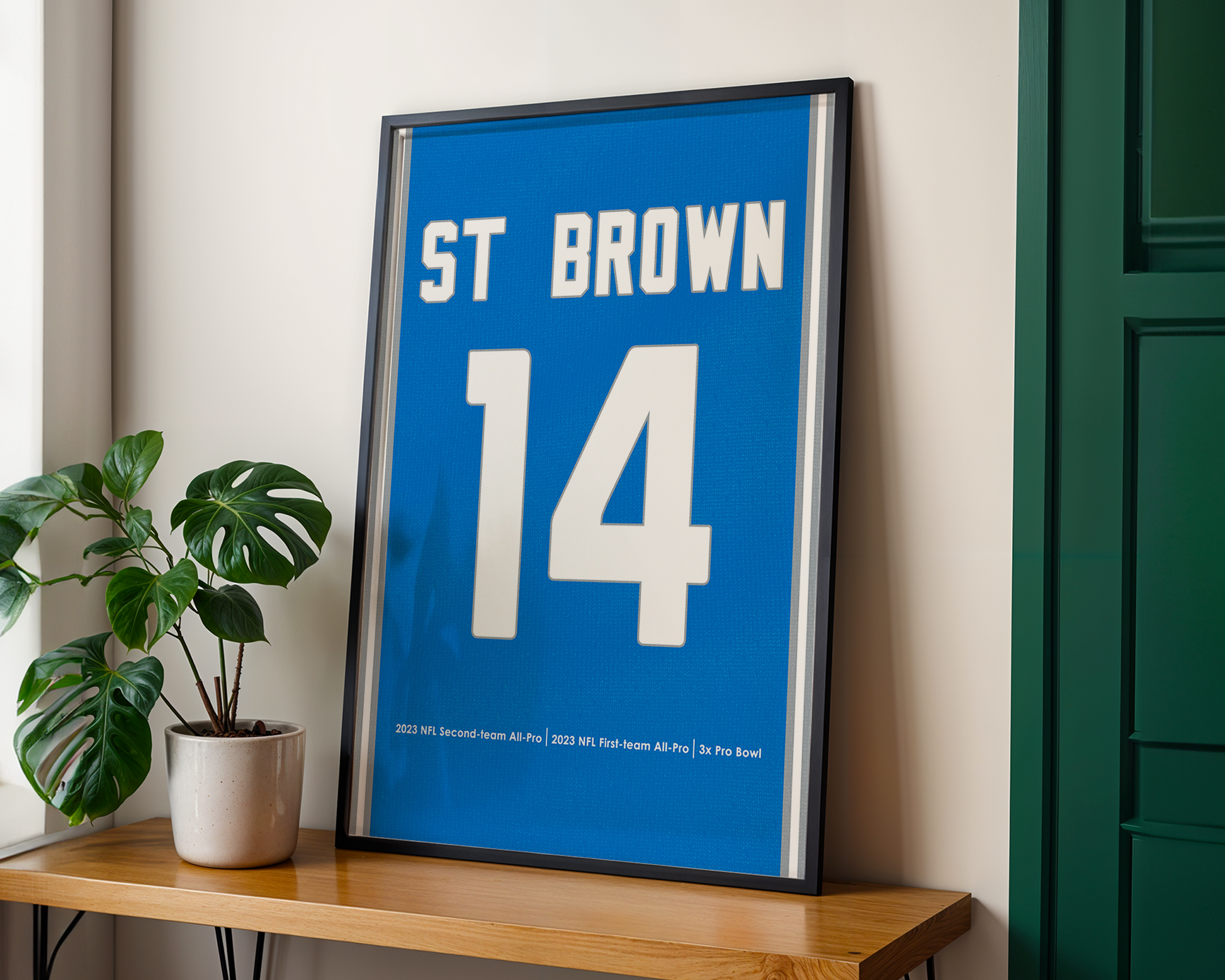 Framed sports jersey with 'ST BROWN 14' on a wooden shelf with a plant.