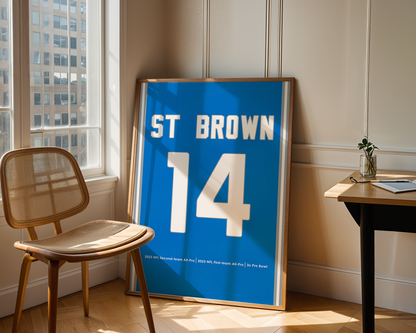 Framed sports jersey with 'ST BROWN 14' on a wall in a room with a chair and table.