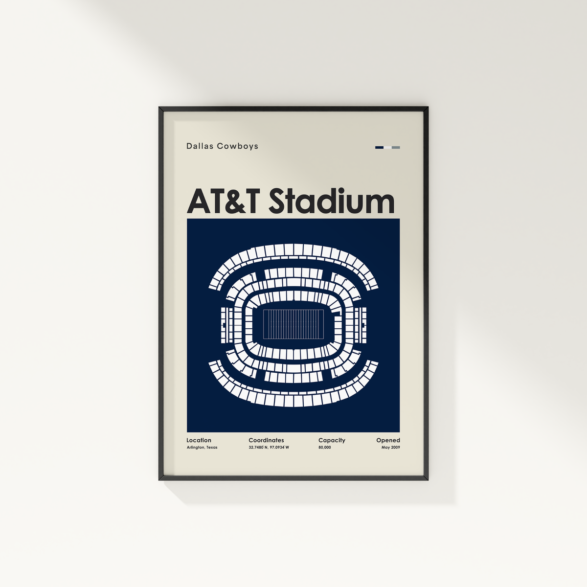 A framed Dallas Cowboys AT&T Stadium poster hangs on a light gray wall. The poster features a navy blue background with a white stadium seating diagram and text including 'Dallas Cowboys', 'AT&T Stadium', and stadium details at the bottom.