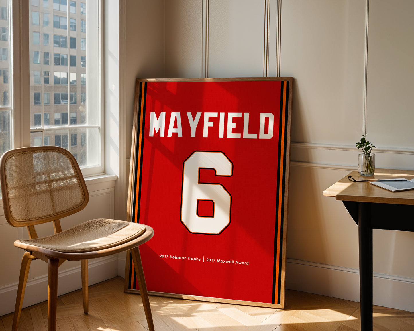 Red sports jersey with 'MAYFIELD 6' on a stand in a room with a chair and table.
