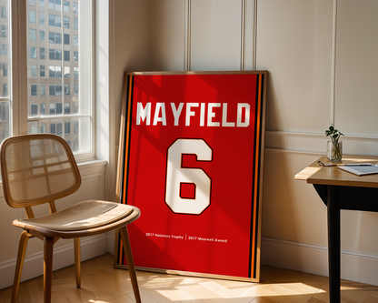 Red sports jersey with 'MAYFIELD 6' on a stand in a room with a chair and table.