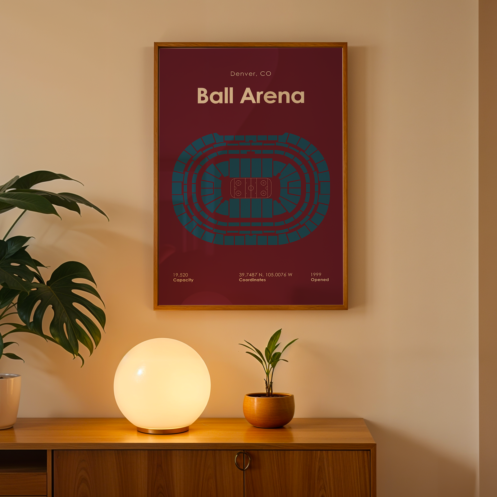 Framed poster of Ball Arena in Denver, CO on a wall with a plant and lamp below.