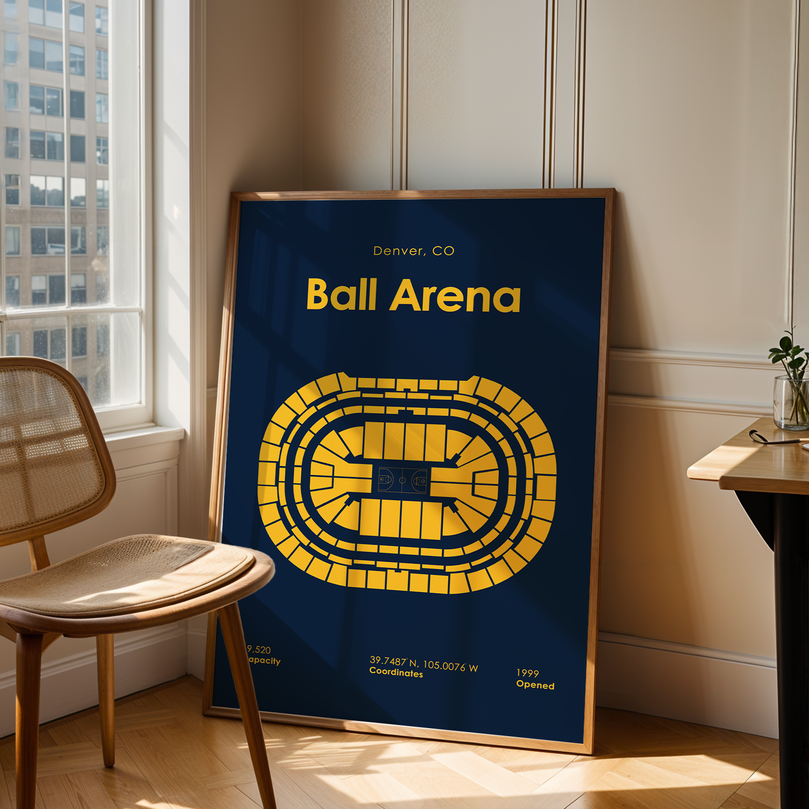 Framed poster of Ball Arena in Denver, CO on a wall next to a chair and table.