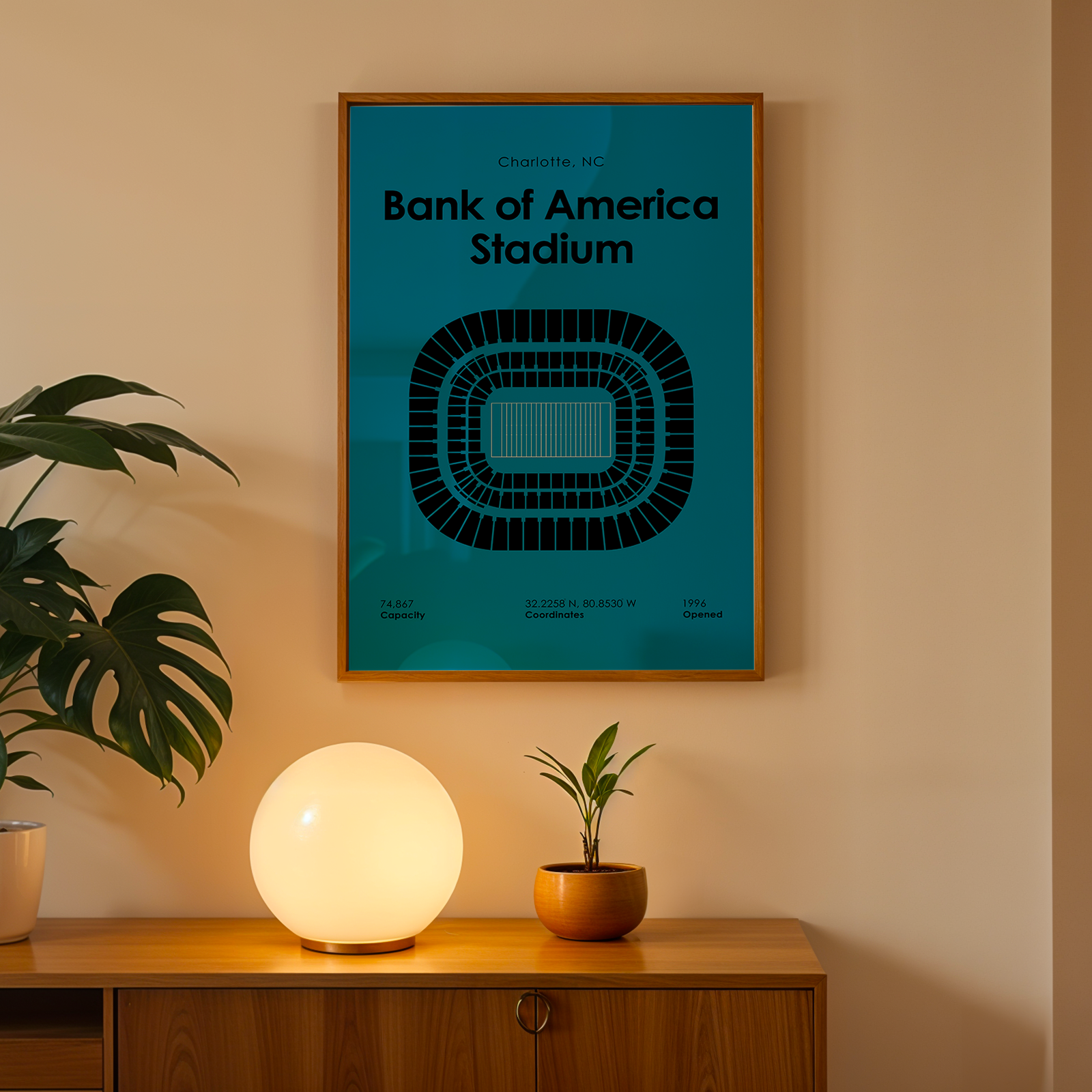 Framed poster of Bank of America Stadium on a wall above a wooden cabinet with decorative items.