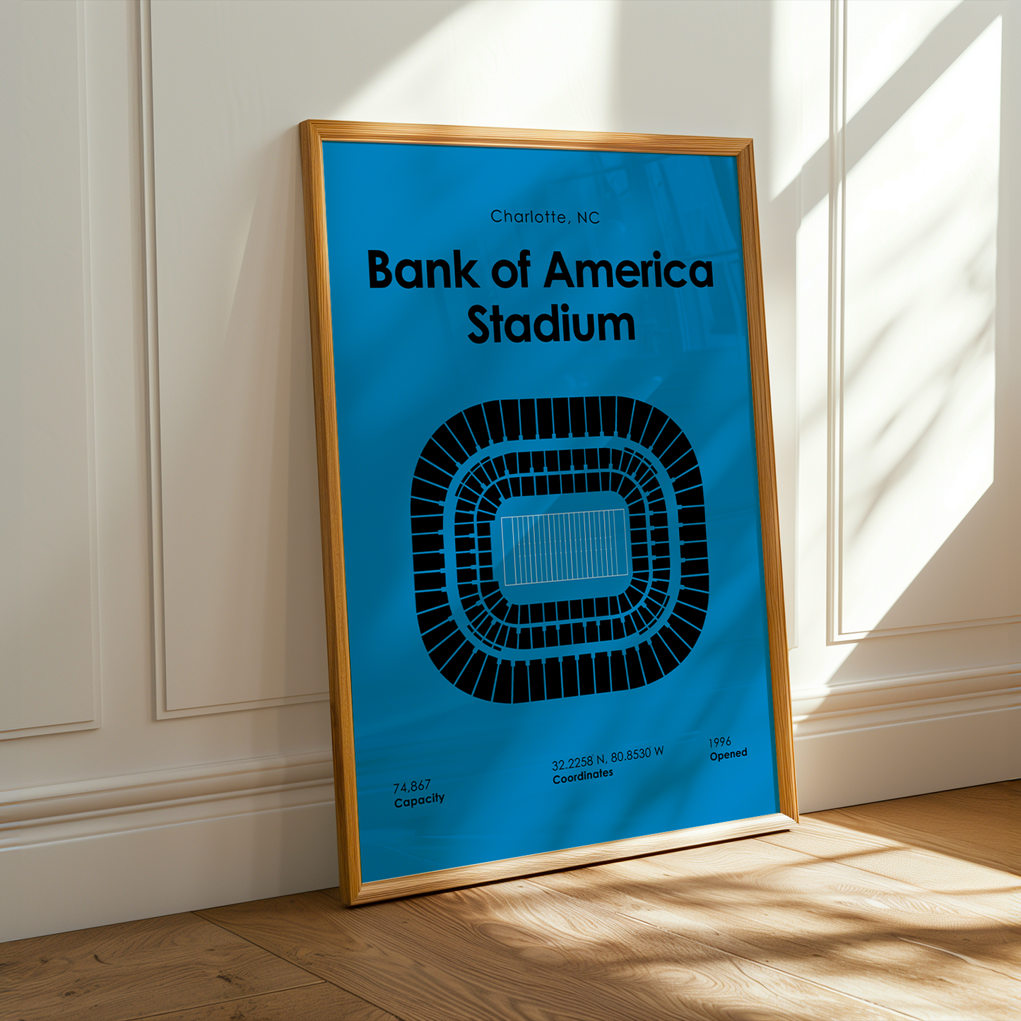 Framed poster of Bank of America Stadium on a wall with sunlight casting shadows.