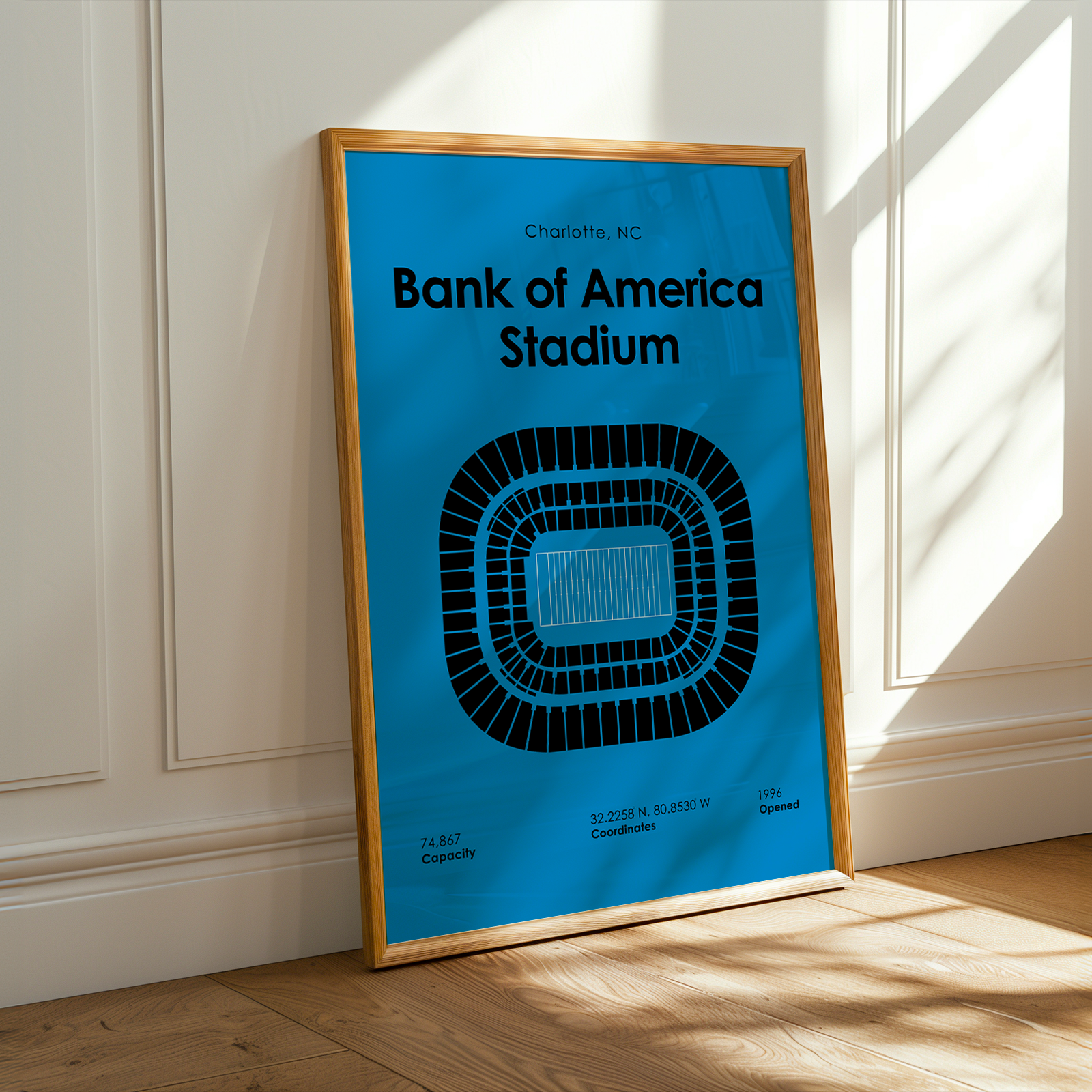 Framed poster of Bank of America Stadium on a wall with sunlight casting shadows.