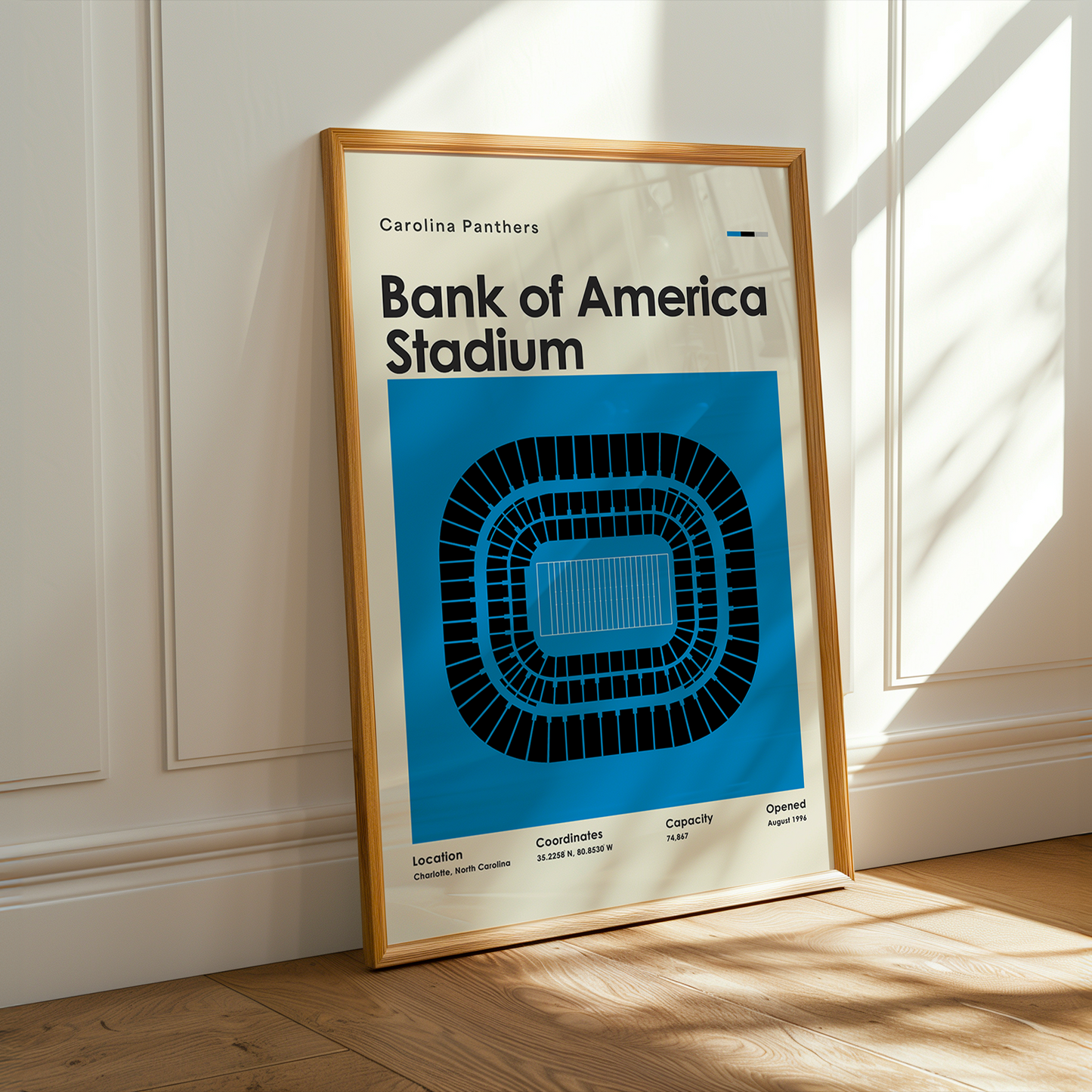 Framed poster of Bank of America Stadium on a wooden floor with sunlight streaming through a window.