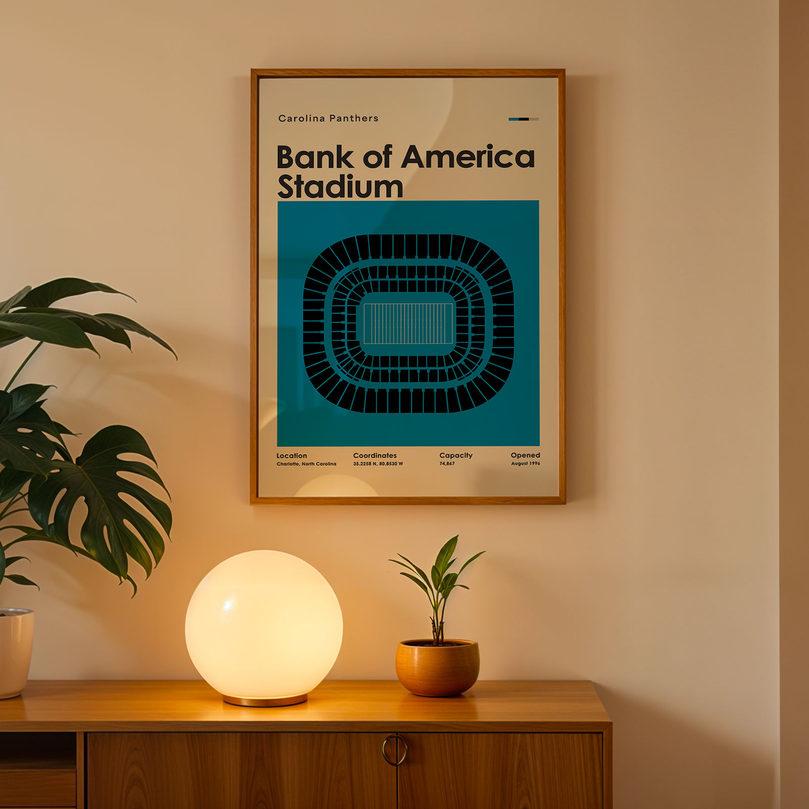 Framed poster of Bank of America Stadium on a wall above a wooden cabinet with decorative items.