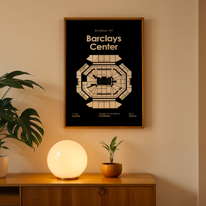 Framed Barclays Center map on a wall with a plant and lamp on a wooden table below.
