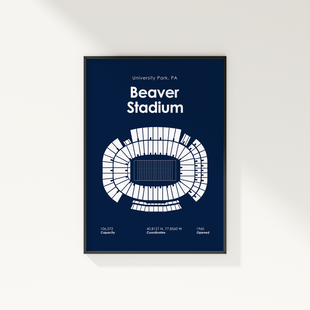 A framed poster of Beaver Stadium in University Park, PA, featuring a white stadium floor plan and text on a dark navy blue background, shown hanging on a light beige wall.