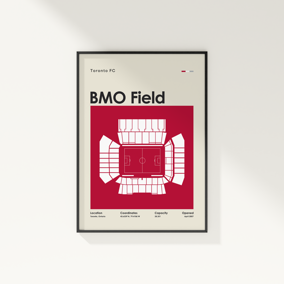 A framed minimalist sports poster of BMO Field from Toronto FC, featuring a white stadium floor plan on a deep red background, mounted on a light gray wall.