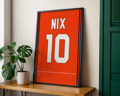Framed poster with 'NIX' and number '10' on an orange background, placed on a wooden shelf.