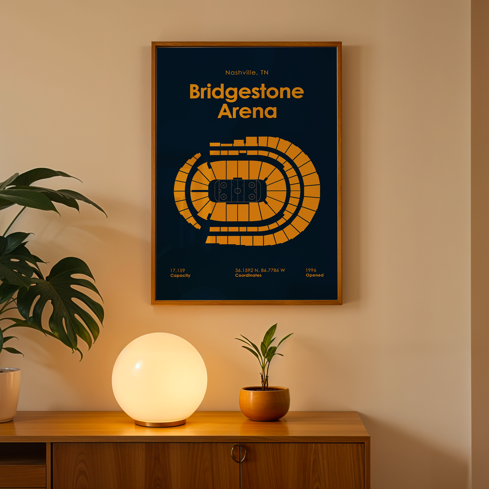 Framed poster of Bridgestone Arena on a wall with a plant and lamp below.
