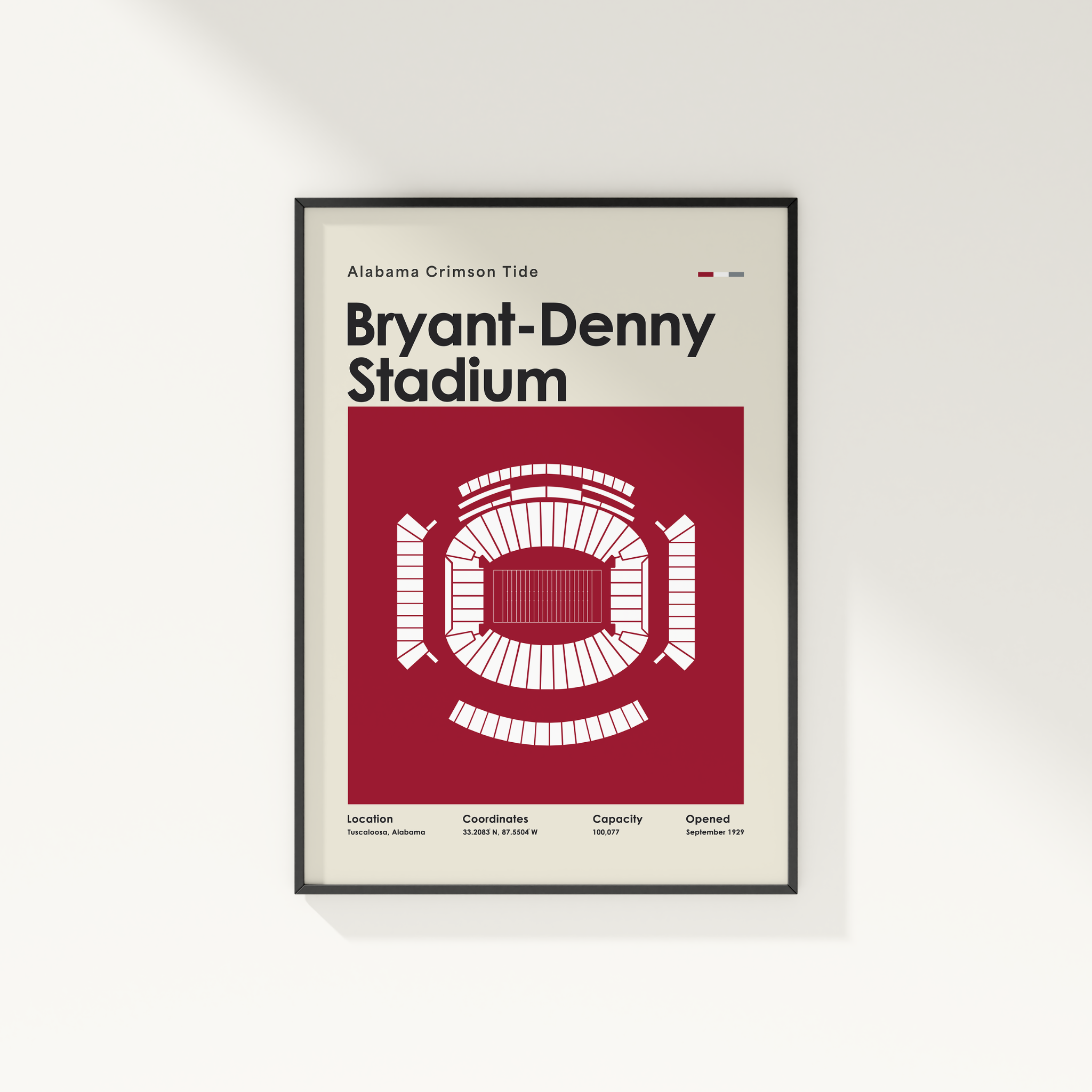 A framed poster of Bryant-Denny Stadium from the Alabama Crimson Tide, featuring a clean graphic design with a red and white stadium layout on a cream background, displayed on a light gray wall.
