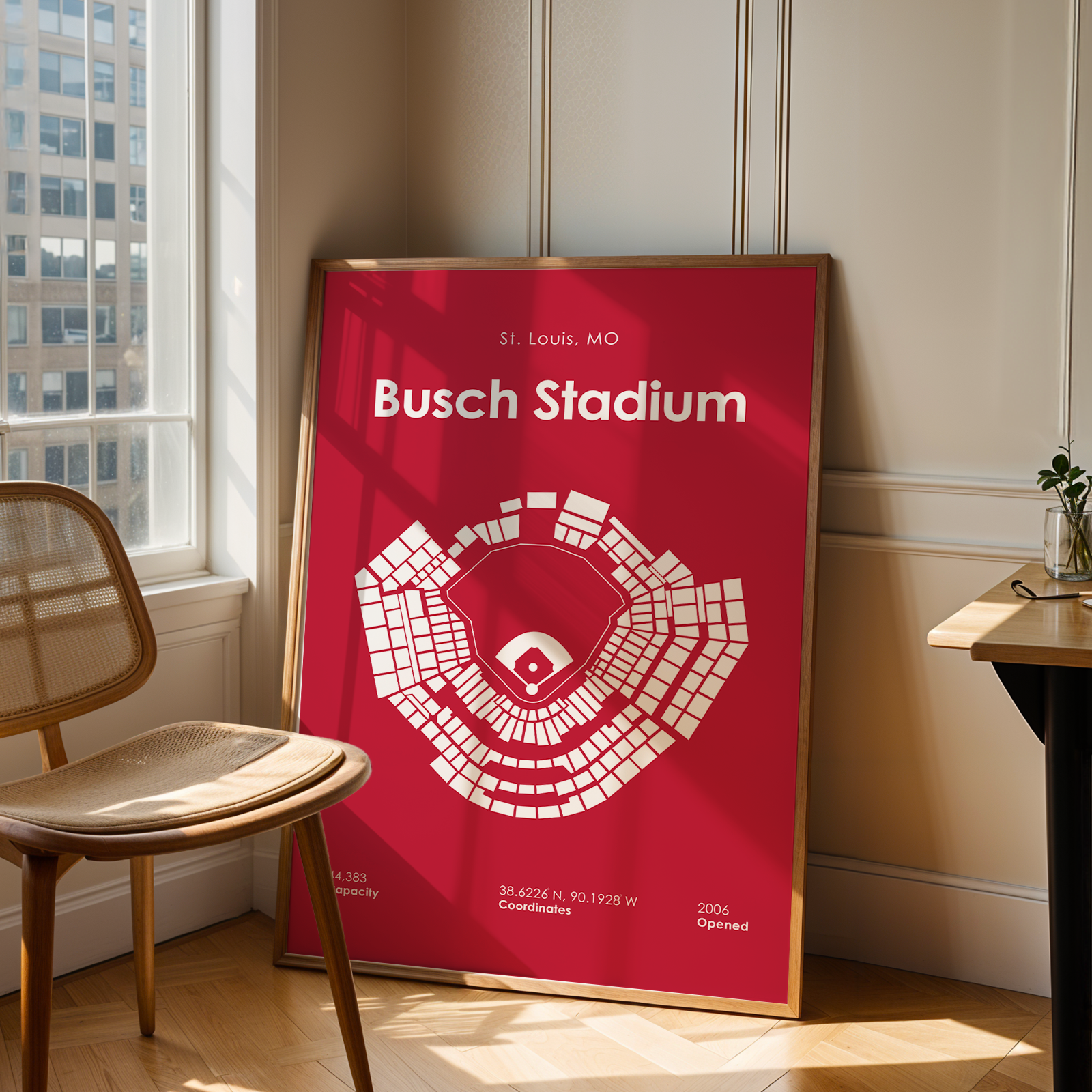 Framed poster of Busch Stadium in a room with a window and chair.