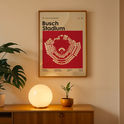 Framed poster of Busch Stadium above a wooden cabinet with decorative plants and a lamp.