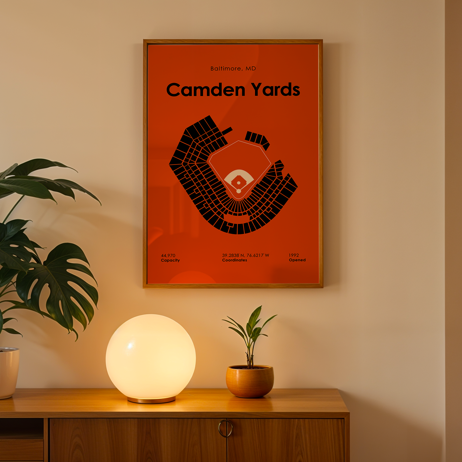 Framed 'Camden Yards' poster on a wall with a lamp and plant below.