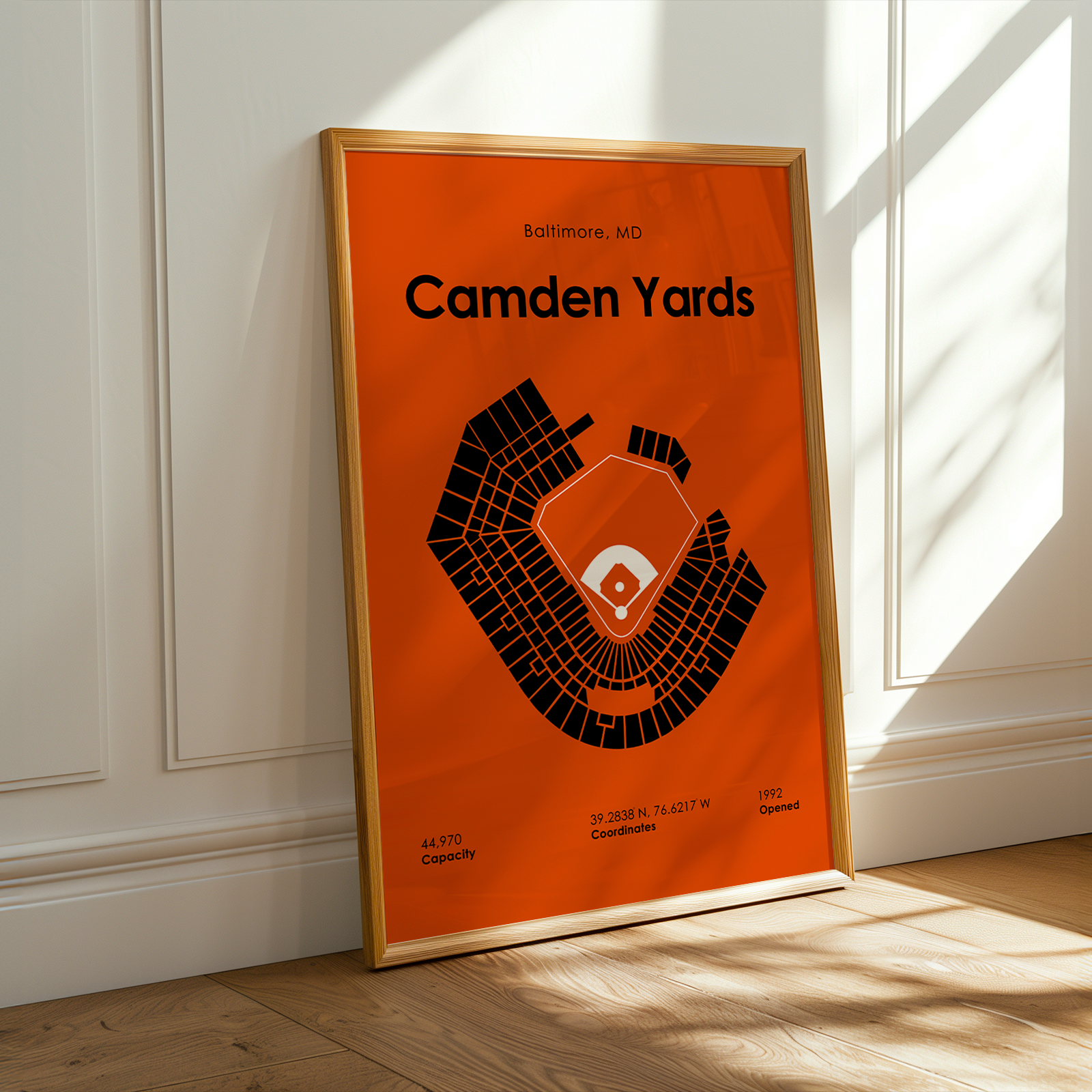 Framed poster of Camden Yards with orange background and black text on a wall.