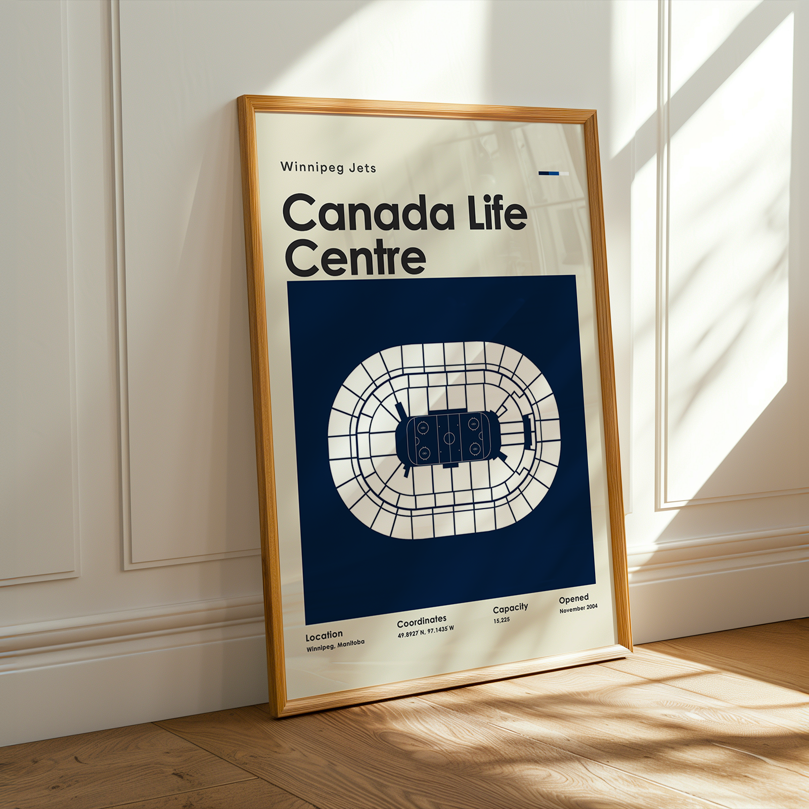 Framed poster of Canada Life Centre with wooden frame on a light-colored wall.