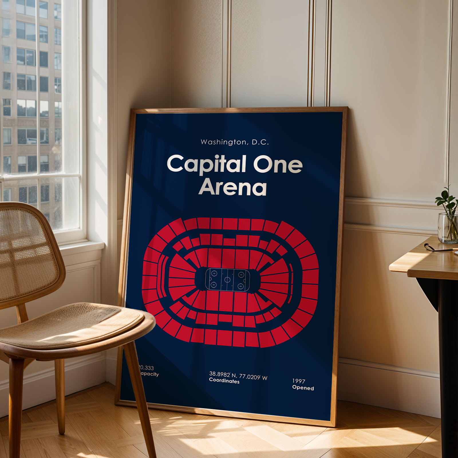 Framed poster of Capital One Arena in Washington, D.C. on a wall in a room with a chair and window.