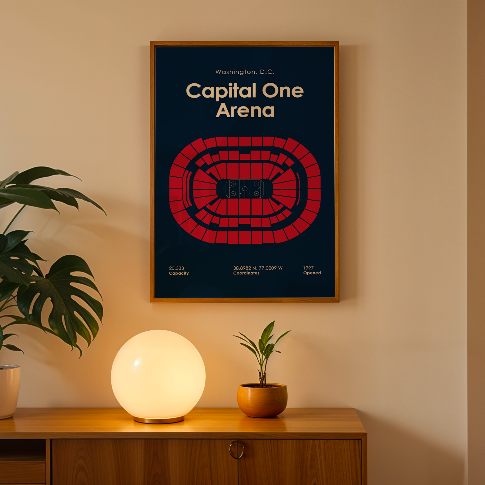 Framed poster of Capital One Arena on a wall with a plant and lamp below.