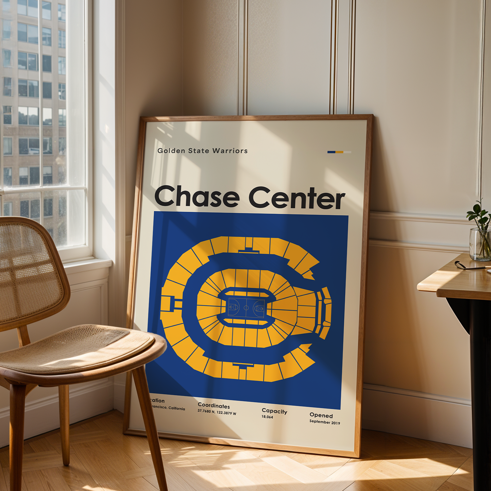 Framed poster of the Golden State Warriors' Chase Center in a room with a chair and window.