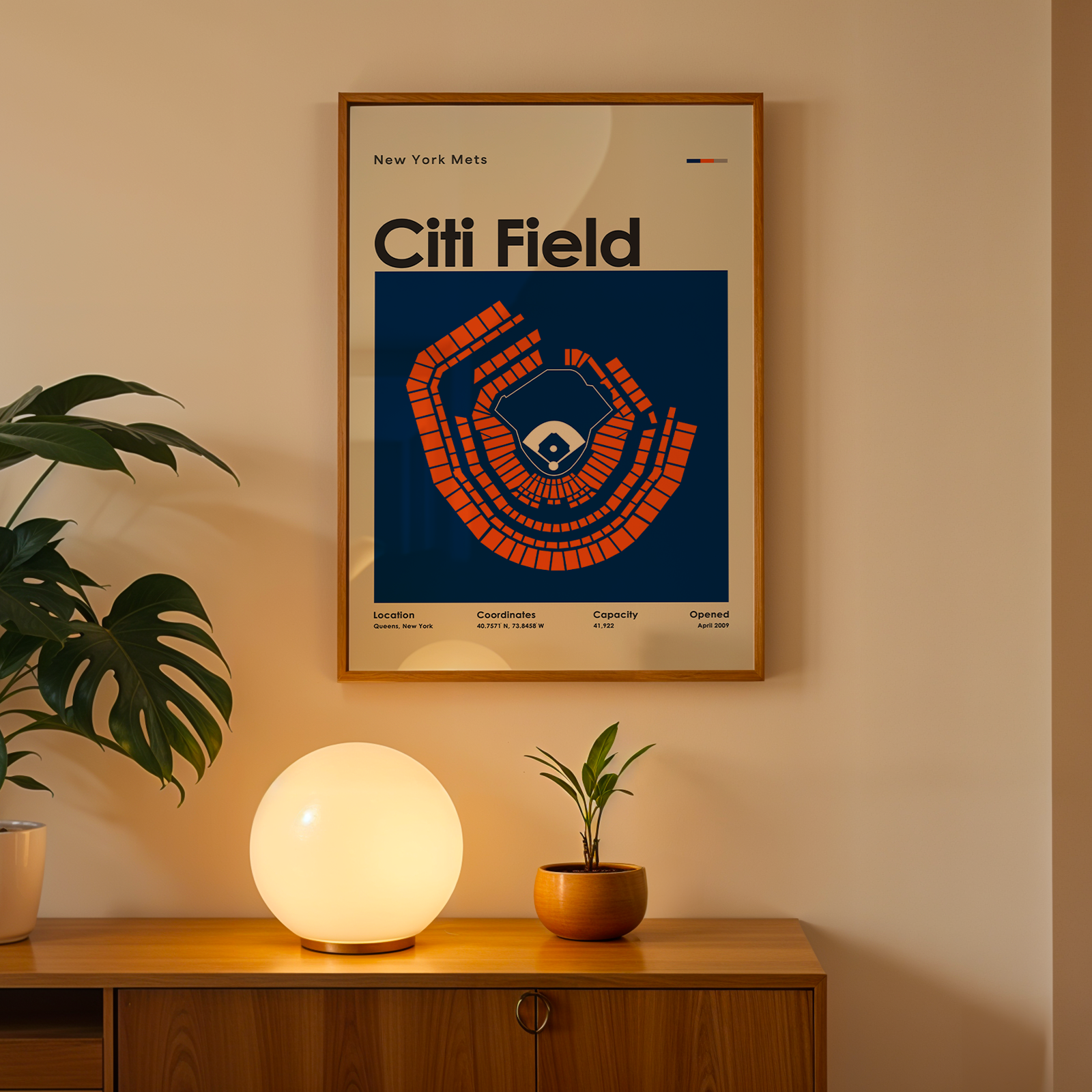 Framed poster of Citi Field on a wall above a wooden cabinet with decorative plants and a lamp.